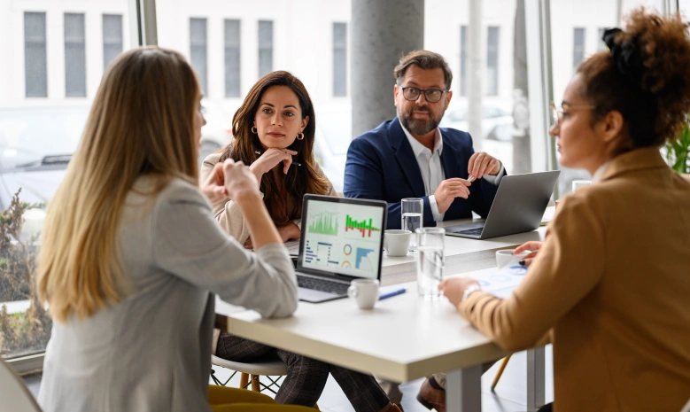 Businesswoman reviewing report on her laptop while discussing business growth with coworkers in meeting